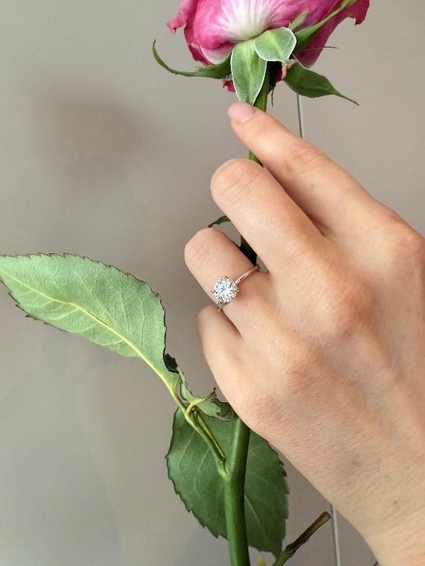 Main portant une bague de promesse solitaire en diamant tenant une rose.