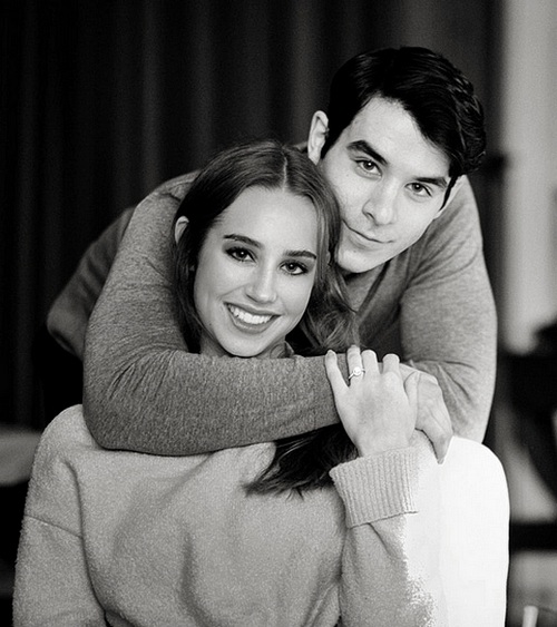 Jeune femme posant avec sa bague de fiançailles solitaire en diamant aux côtés de son fiancé.