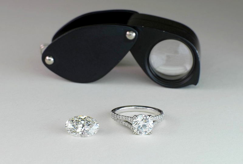 Loupe de diamantaire devant diamant et bague de fiançailles.